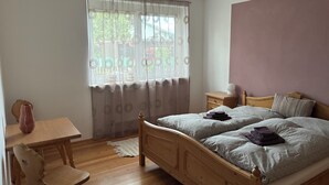 Um quarto com cama de madeira, uma pequena mesa de cabeceira, uma cadeira e uma janela com cortinas.