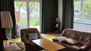 Sala de estar com dois sofás de couro marrom, uma mesa de centro de madeira, uma luminária e vista para o exterior através de amplas janelas.