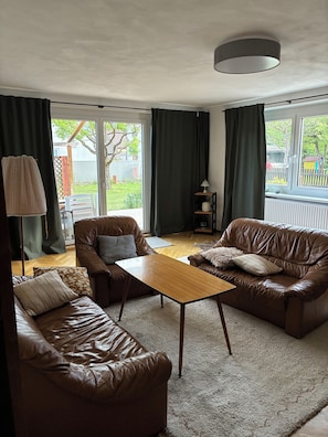 Un salon avec deux canapés en cuir marron, une table basse en bois, une lampe et une vue sur l’extérieur grâce à de grandes fenêtres.