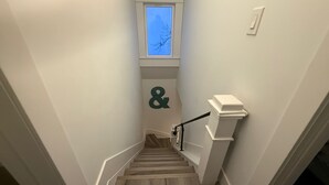 Una escalera estrecha con barandilla, una ventana con vistas a un árbol y un enchufe en la pared.