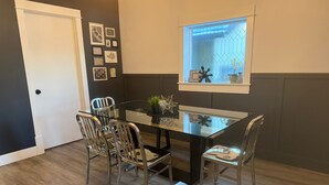 Un comedor con mesa de vidrio y sillas de metal, una puerta y una ventana con vistas.