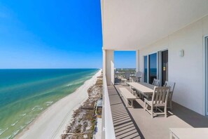 Un balcone con vista sulla spiaggia e sull'oceano, un tavolo con sedie e una facciata di un edificio moderno.