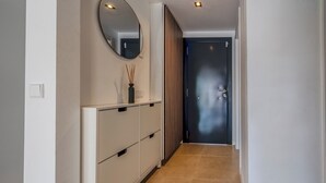 Un pasillo con un armario blanco, un espejo, un florero con cañas, una puerta con manija y un accesorio de iluminación en el techo.