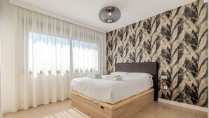 Un dormitorio con cama, cortinas blancas, pared estampada y luz en el techo.