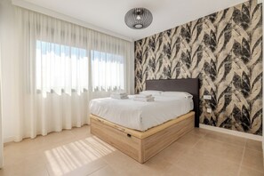 Ein Schlafzimmer mit einem Bett, weißen Vorhängen, einer Wand mit Muster und einer Deckenleuchte.