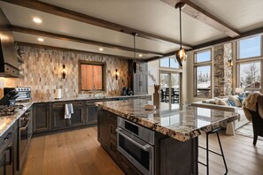 A spacious kitchen with granite countertops, a large island, and a stone accent wall. - *New Build* Black Eagle Ski-In/Ski-Out Retreat (Big Sky)