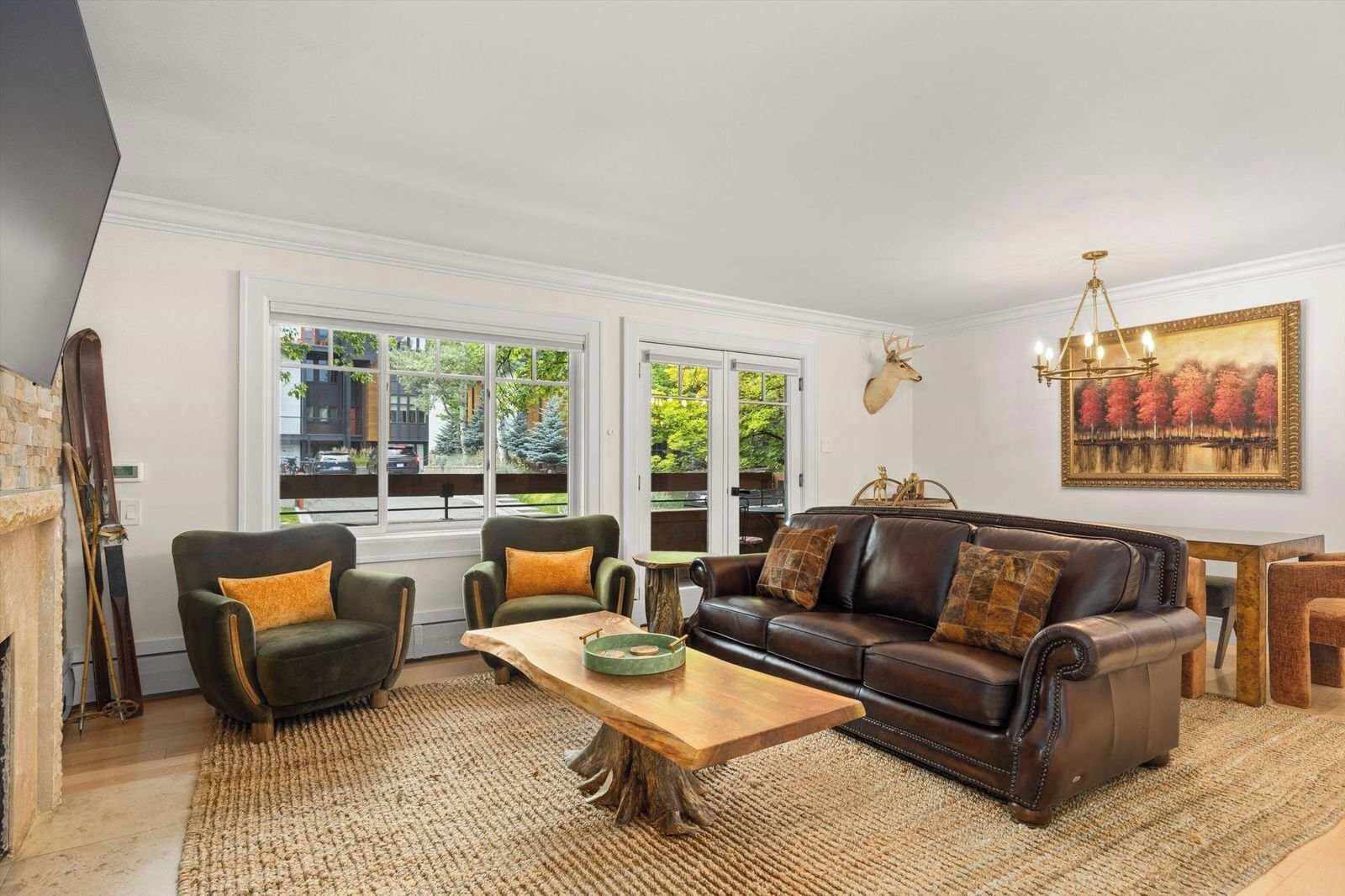 A living room with a fireplace, leather sofa, and a large window with a view of trees.