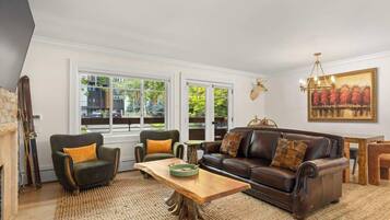 A living room with a fireplace, leather sofa, and a large window with a view of trees.