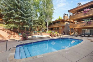 A swimming pool with a stone border, surrounded by lounge chairs and a wooden deck.