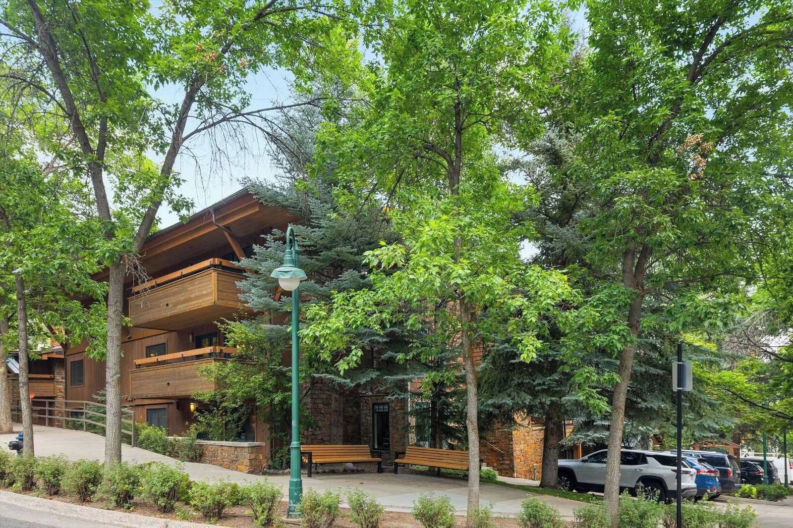 Un edificio a più piani con facciata in legno, ingresso in pietra e una panchina di fronte.