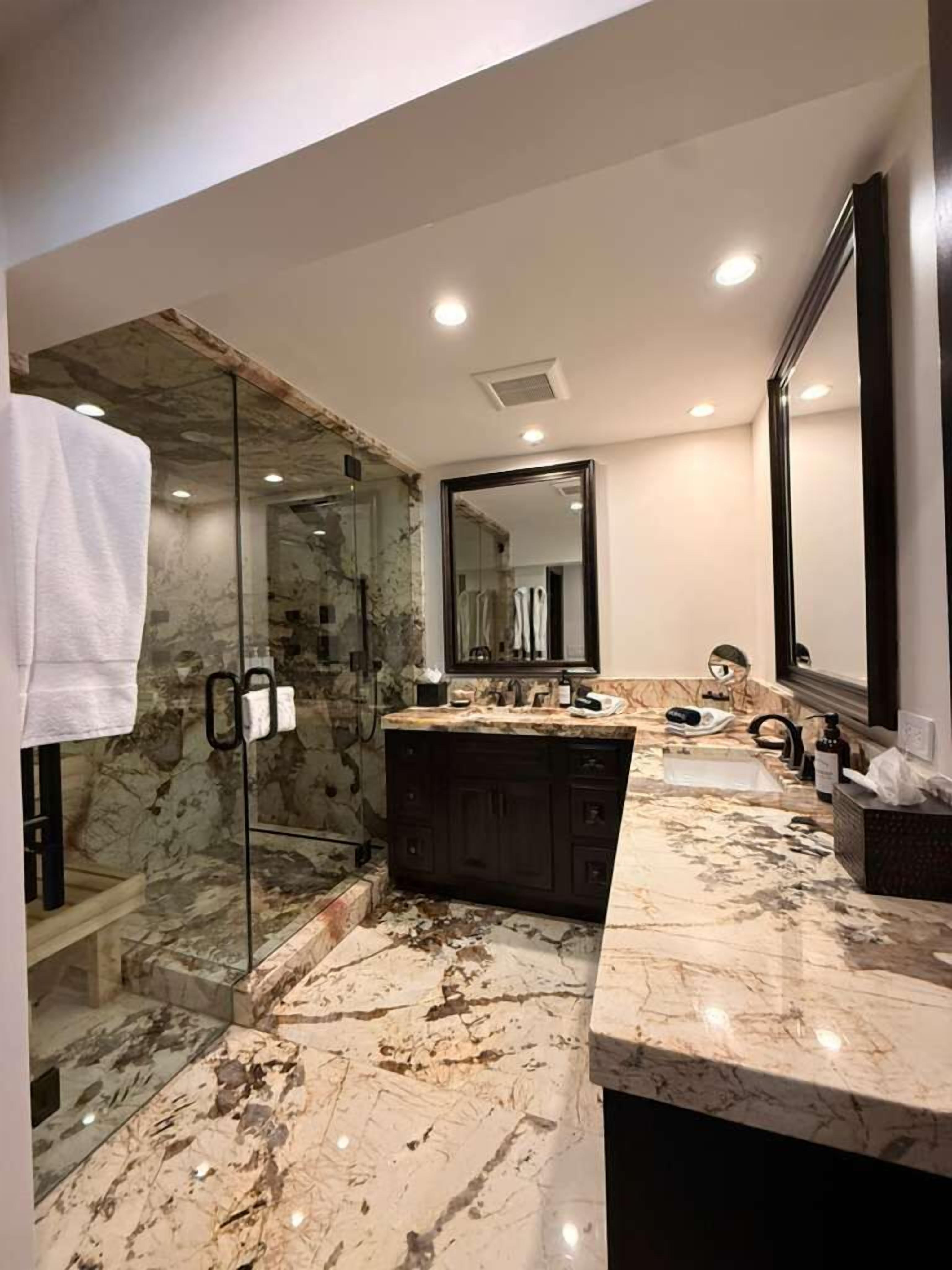 Un baño con ducha de vidrio, tocador de mármol y un espejo grande.