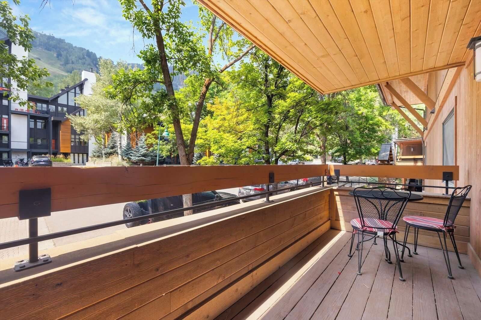 A wooden deck with a table and chairs, overlooking a street and trees.