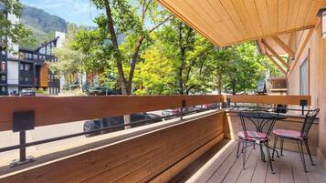 A wooden deck with a table and chairs, overlooking a street and trees.