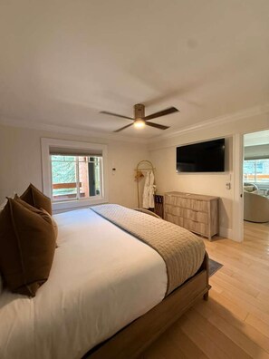 A bedroom with a bed, a ceiling fan, a TV, and a view of the outdoors.
