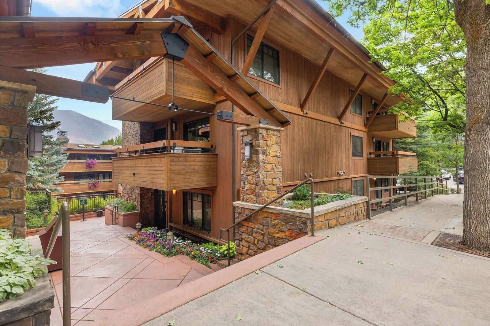 A multi-story wooden building with balconies, stone accents, and a landscaped garden area.