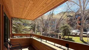 Une terrasse en bois dotée d’une rambarde, de bancs et offrant une vue sur une zone boisée et des bâtiments.