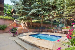 A swimming pool with a stone deck, surrounded by a garden with various plants and flowers, and a staircase leading to an upper level.
