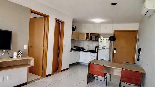 A modern kitchen with white cabinets, a dining area with a wooden table and two chairs, and a living room with a sofa. - Flat 106 S Iloa Residence - Barra de São Miguel, Alagoas, vacation rental (Barra de São Miguel)
