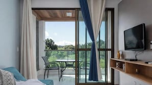 A room with a bed, a TV, a table with chairs, and a balcony with a view. - Flat 106 S Iloa Residence - Barra de São Miguel, Alagoas, vacation rental (Barra de São Miguel)