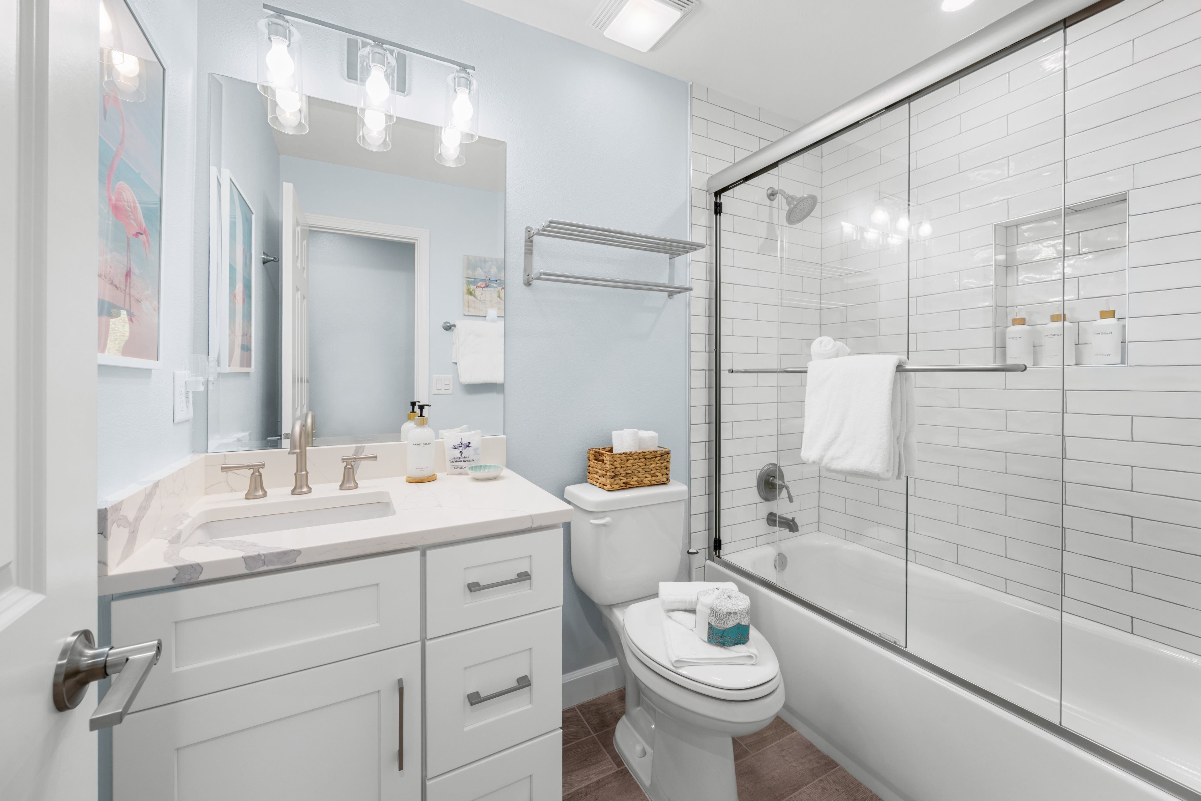 A modern bathroom with a glass shower enclosure, a white vanity with drawers, a toilet, and a large mirror.
