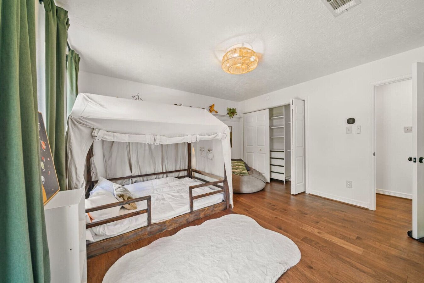 Una habitación con una cama de madera, ropa de cama blanca, una alfombra blanca, una lámpara de techo y un armario con espejo.
