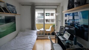 A compact room with a bed, a desk with a laptop, a chair, and a balcony with a view of the outside. - Parisian studio in the 17th district, fully equipped with balcony (Paris)