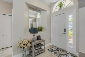 A hallway with a white door, a console table with a lamp, a vase of flowers, and a welcome bag. - Private Pool Retreat / Pet-Friendly / Sleeps 6 (Port Orange)