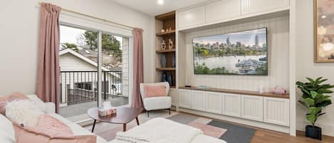 Un salon moderne avec un canapé, une table basse, un téléviseur fixé au mur et une vue sur le paysage urbain par la fenêtre.