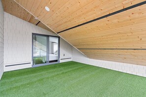 A room with a sloped wooden ceiling, white brick walls, and a green artificial turf floor. - Brand-New Sun-Drenched Kits Home - Rooftop Deck (Vancouver)