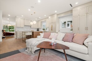 Eine moderne Küche mit weißen Schränken, eine Essecke mit einem weißen Tisch und ein Wohnzimmer mit einem weißen Sofa und einem Couchtisch.