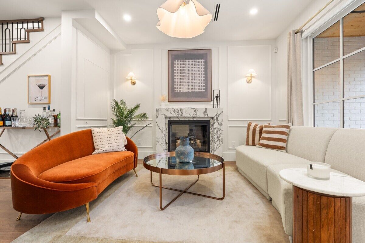 A modern living room with a fireplace, a sofa, a coffee table, and a staircase.