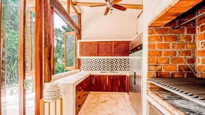 A kitchen with a brick oven, wooden cabinets, and a view of greenery. - Kasa Uh May (Francisco Uh May)