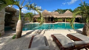 A pool area with lounge chairs, a thatched-roof structure, and a palm tree. - Kasa Uh May (Francisco Uh May)