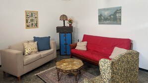 A living room with a beige sofa, a red sofa, a patterned armchair, a small round coffee table, a blue cabinet with a lamp, and a painting on the wall. - Casita on quiet street just 15 minute walk to historic center. (Oaxaca de Juárez)