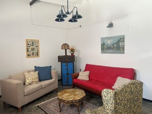 Ein Wohnzimmer mit einem beigefarbenen Sofa, einem roten Sofa, einem gemusterten Sessel, einem kleinen runden Couchtisch, einer blauen Kommode mit einer Lampe und einem Gemälde an der Wand.