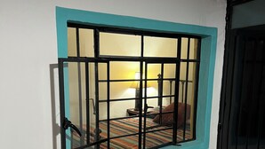 A window with a metal grille, a bed with a striped bedspread, and a lamp in the background. - Casita on quiet street just 15 minute walk to historic center. (Oaxaca de Juárez)