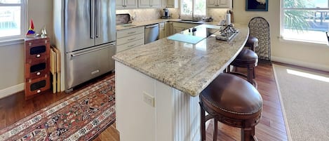 A kitchen with a large island, stainless steel appliances, and a view of the outdoors.