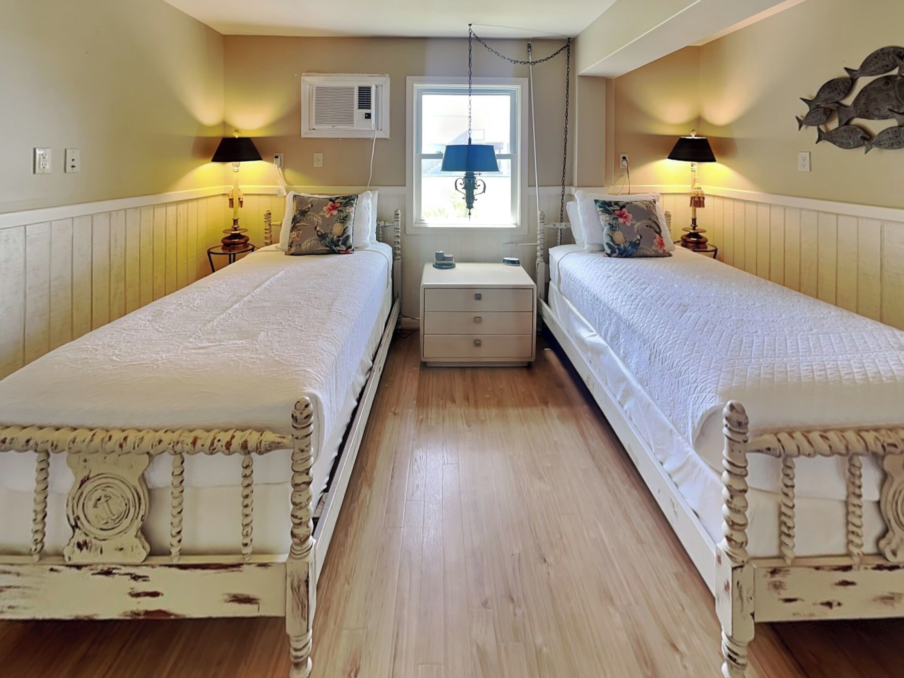 A bedroom with two beds, a nightstand, a lamp, a window, and a wall decoration.