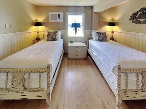 Un dormitorio con dos camas, una mesita de noche, una lámpara, un ventanal y un adorno en la pared.