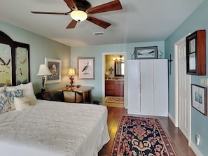 A bedroom with a bed, a desk, a ceiling fan, and a view into the bathroom. - Galveston Baywatch (Galveston)