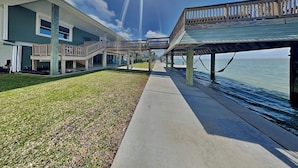 A waterfront property with a covered walkway, a grassy lawn, and a view of the water. - Galveston Baywatch (Galveston)