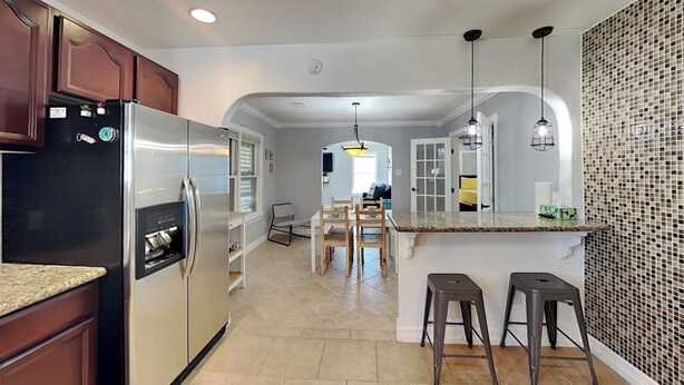 A modern kitchen with a stainless steel refrigerator, a dining area with a table and chairs, and a tiled floor. - Shell City (Galveston)