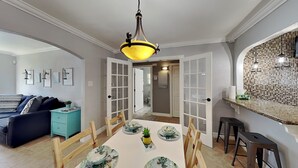 A dining area with a white table, wooden chairs, and a yellow pendant light. - Shell City (Galveston)