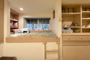 Un lit superposé avec une fenêtre, des étagères en bois ornées de livres et d’objets décoratifs, et une échelle.