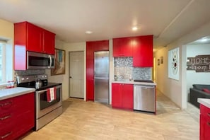 Une cuisine avec des meubles de couleur rouge, des appareils électroménagers en acier inoxydable et un dosseret carrelé.