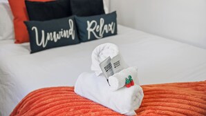 A neatly made bed with a white towel, a red blanket, and pillows with 'Unwind Relax' text. - Modern 3BR Home Game Room Pool & Ping-Pong (Akron)