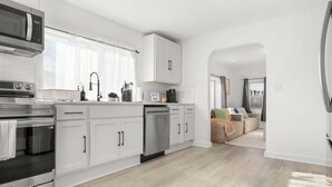 A modern kitchen with white cabinetry, stainless steel appliances, and a view to a living area. - Modern 3BR Home Game Room Pool & Ping-Pong (Akron)