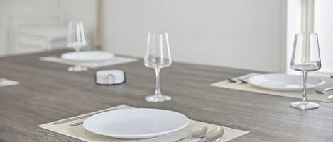 Une table à manger dressée avec de l’argenterie, des assiettes blanches et des verres à vin, le tout sur une table en bois, avec un mur blanc en arrière-plan.