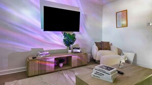 A modern living room with a mounted TV, a sofa, a coffee table, and a console table with decorative items. - Modern 3BR Home Game Room Pool & Ping-Pong (Akron)