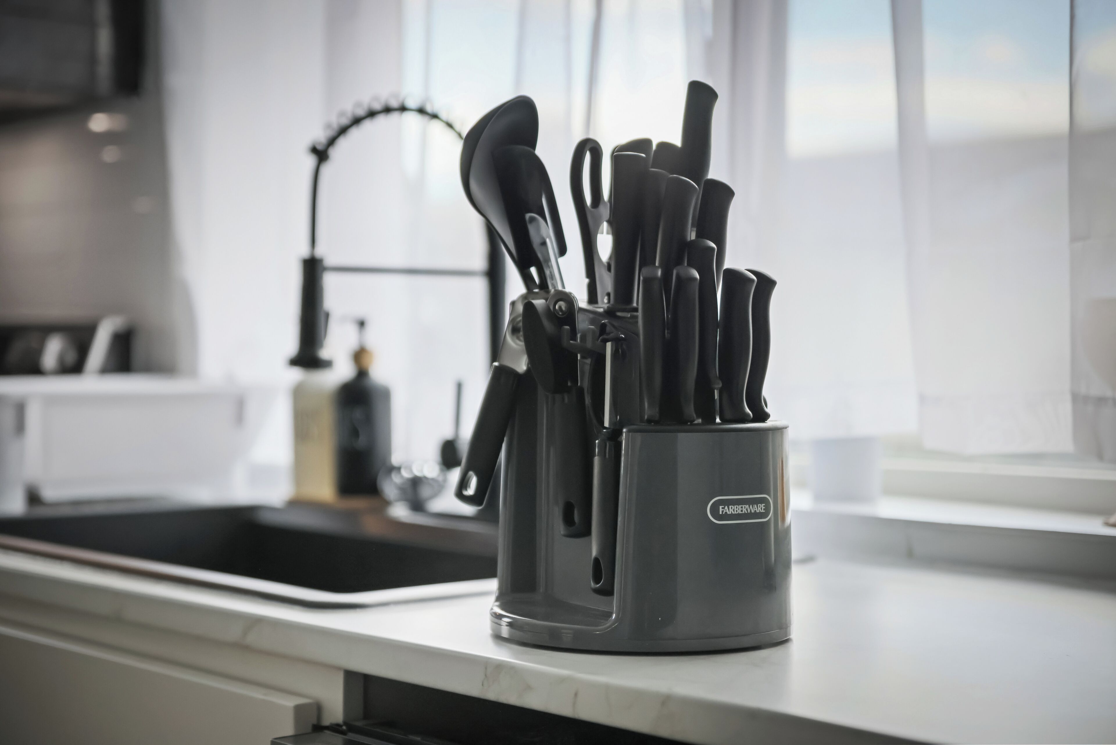 Una cocina con un lavamanos, una llave y un organizador de utensilios en la encimera.